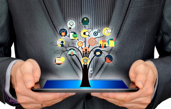 A business consultant holding a tablet with a tree spurting out of its screen with the branches of business growing out of the tree.